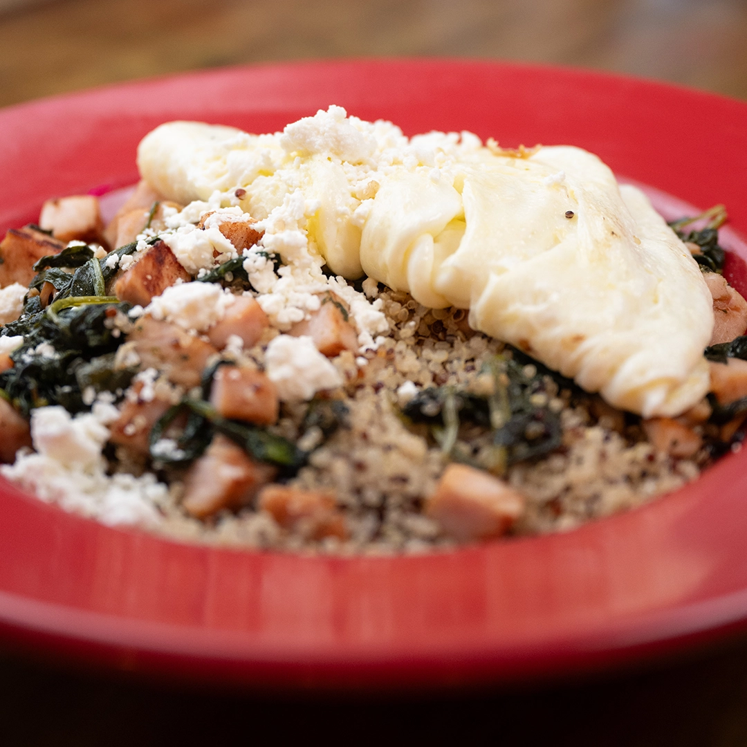 A vibrant red bowl filled with quinoa, smoked turkey, spinach, feta cheese, topped with egg whites