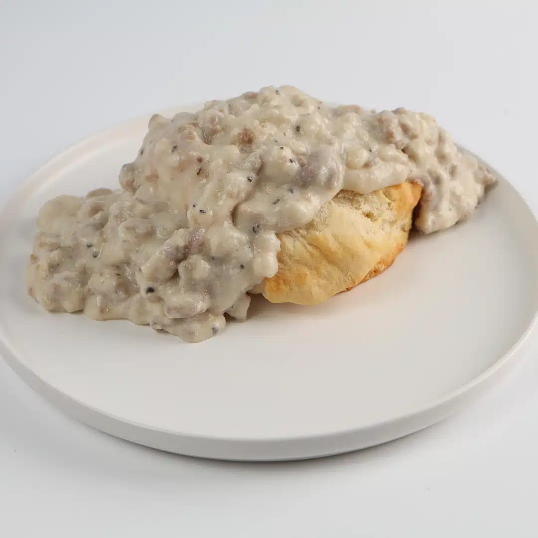 Flaky, golden-brown biscuit topped with creamy sausage gravy on a white plate.