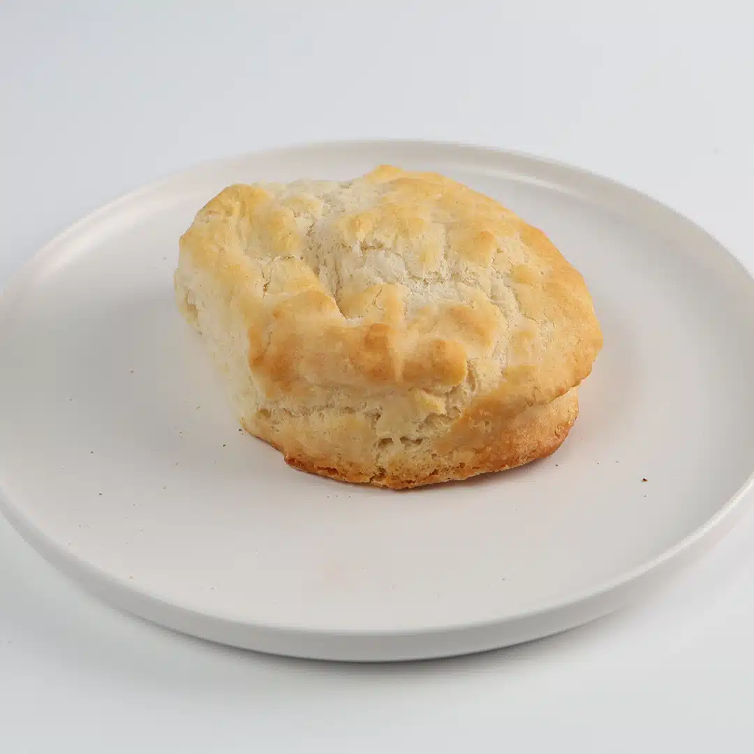 Flaky, golden-brown biscuit on a white plate against a light background.