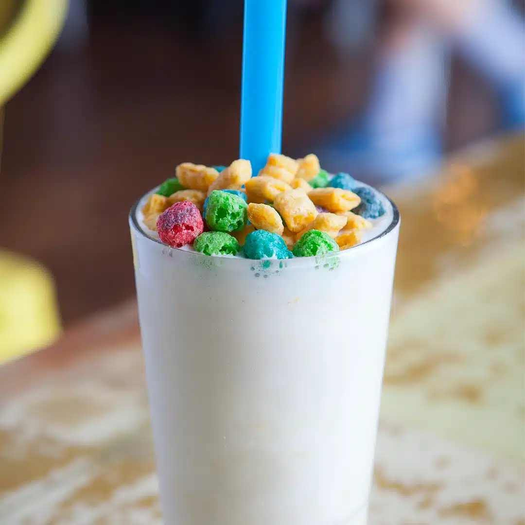 Creamy milkshake topped with colorful cereal pieces, with a large blue straw.