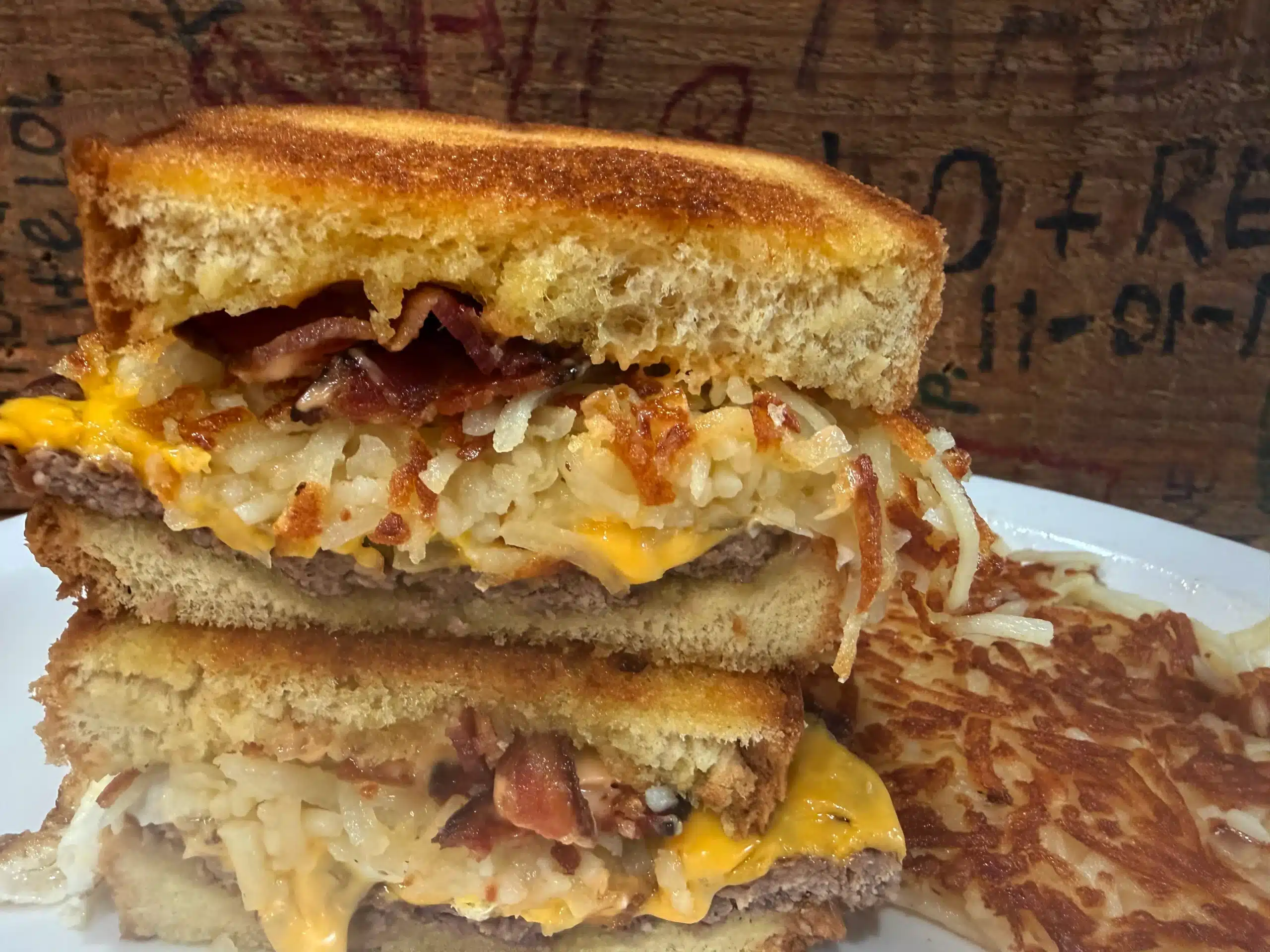 A Breakfast Burger with a smashed patty, American cheese, chopped grilled onion, bacon, Sha'1000 island dressing, fried egg, and hash browns on thick-cut brioche toast.