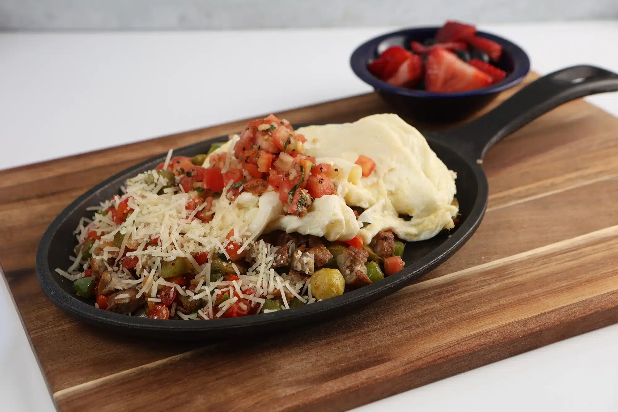 Skillet with roasted Brussels sprouts, peppers, sausage, and egg whites topped with pico de gallo and shaved parmesan, served with a side of mixed berries.