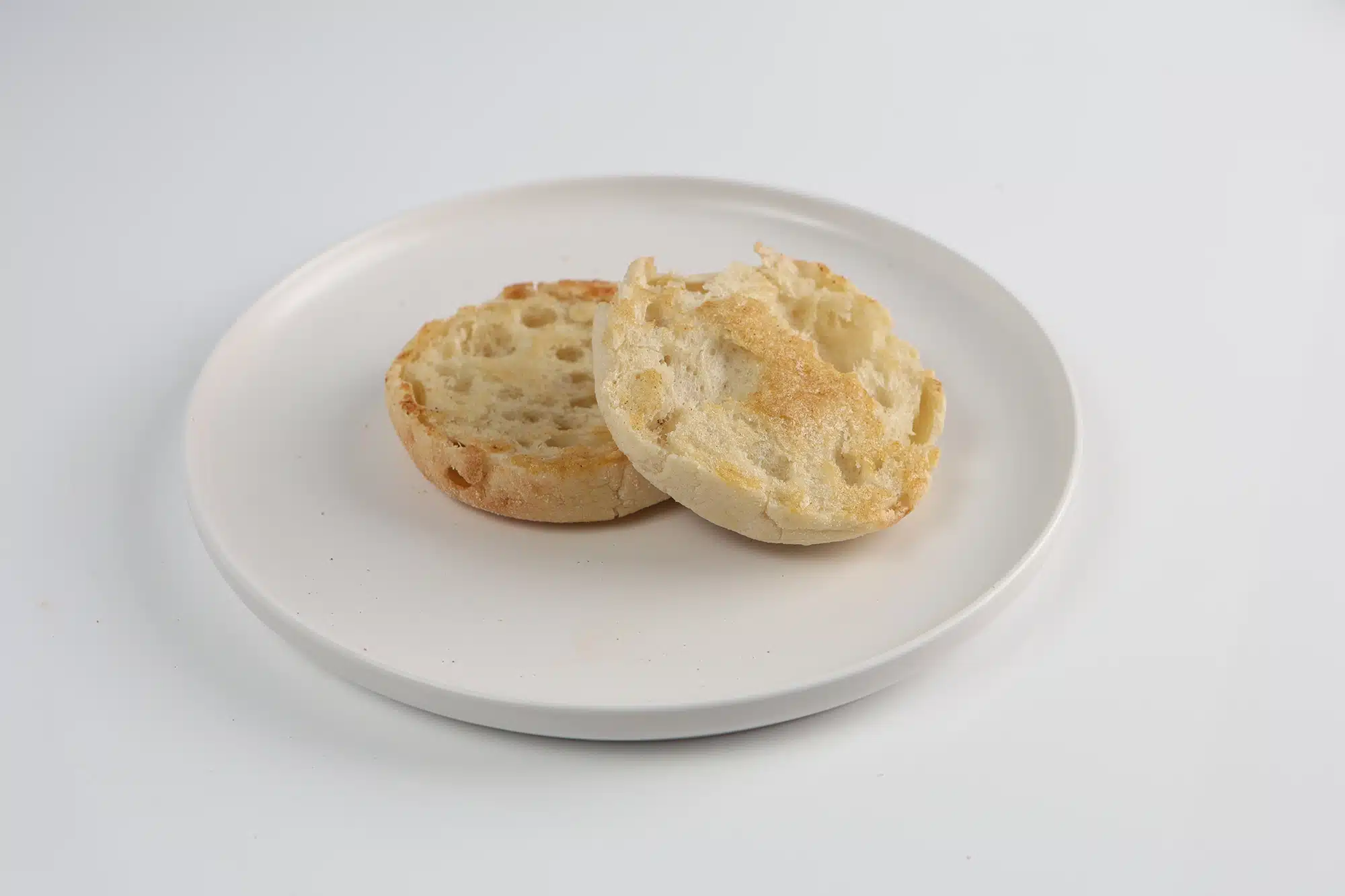Two toasted English muffin halves on a white plate.