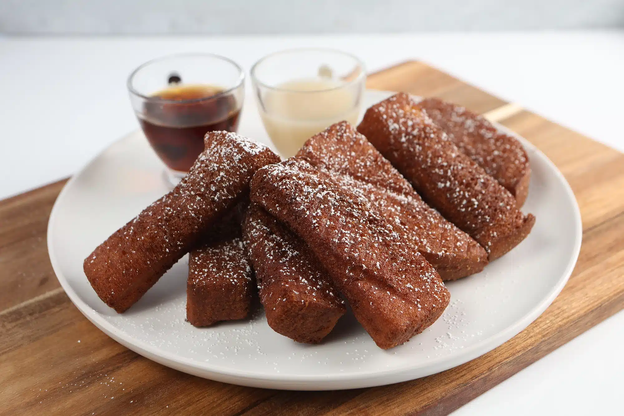 Stack of cinnamon French toast sticks dusted with powdered sugar, served with syrup.