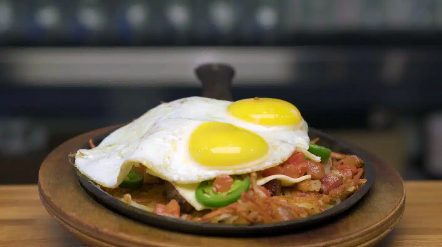 Skillet with crispy hash browns, diced tomatoes, jalapeños, melted cheese, and two sunny-side-up eggs on top.