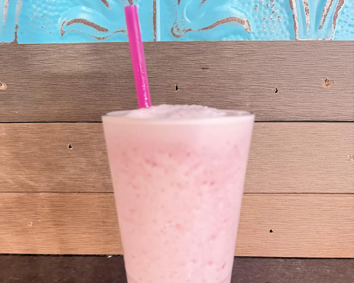 Billy Bob's Straw strawberry smoothie in a tall glass with a pink straw, made with non-fat yogurt.