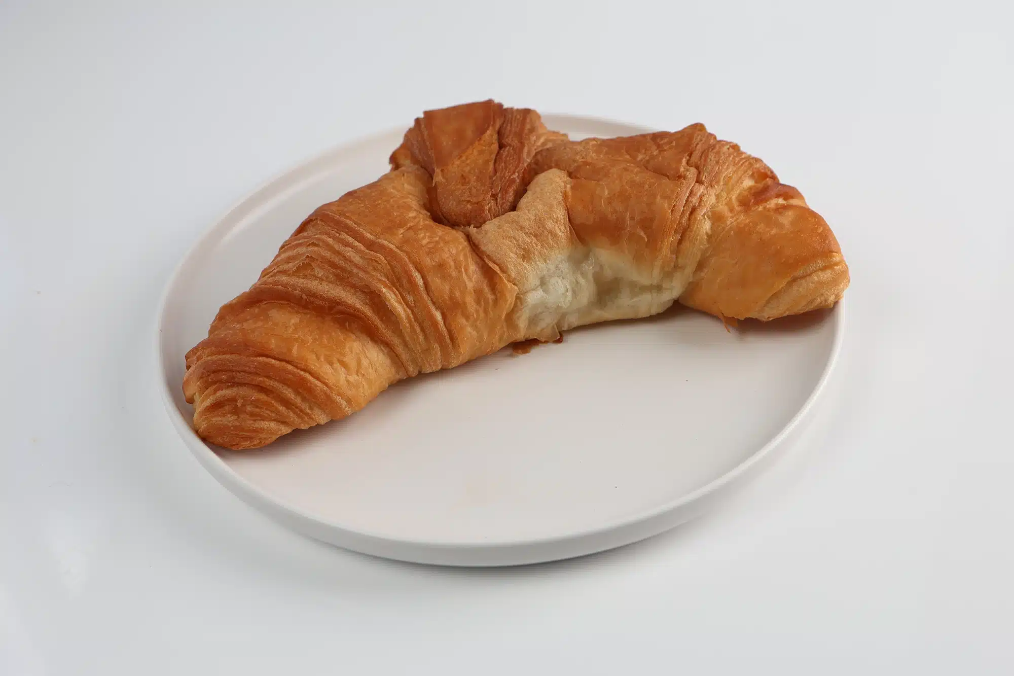 A golden, flaky butter croissant on a white plate.