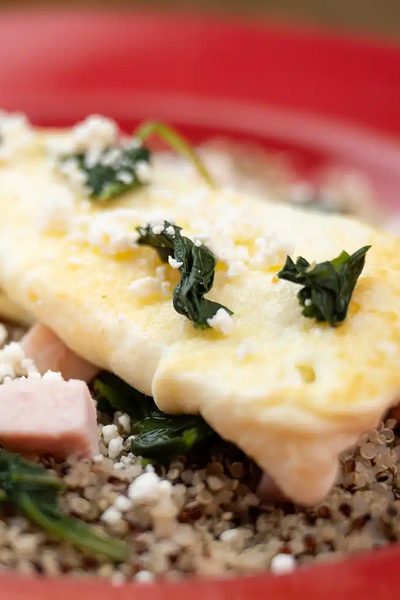 A folded omelette with spinach and feta on a red plate, served with a grain bowl.