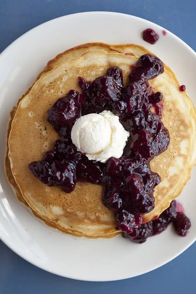 A stack of pancakes under blueberry compote and whipped cream.